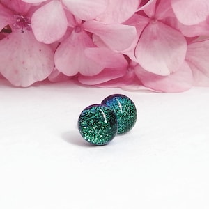 May include: A pair of green and blue iridescent glass stud earrings. The earrings are round and have a textured surface.