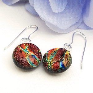 May include: A pair of silver dangle earrings with round, iridescent glass drops. The glass is a deep red with streaks of blue, green, and gold.