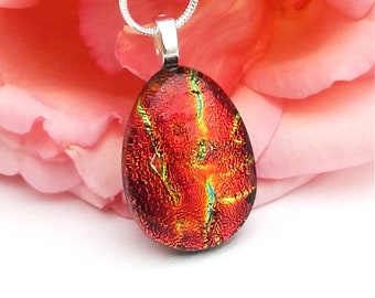 May include: A red glass pendant with iridescent gold and green accents hangs from a silver chain. The pendant is oval shaped and has a textured surface.
