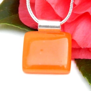 May include: A silver chain necklace with a square orange glass pendant.