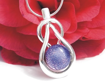 Könnte beinhalten: Eine silberne Halskette mit einem Anhänger in Form eines Knotens und einer violetten Glaskugel in der Mitte. Die Kugel hat eine strukturierte Oberfläche.