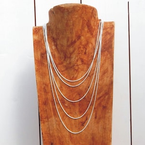 May include: A set of six silver chain necklaces of varying lengths displayed on a wooden mannequin.