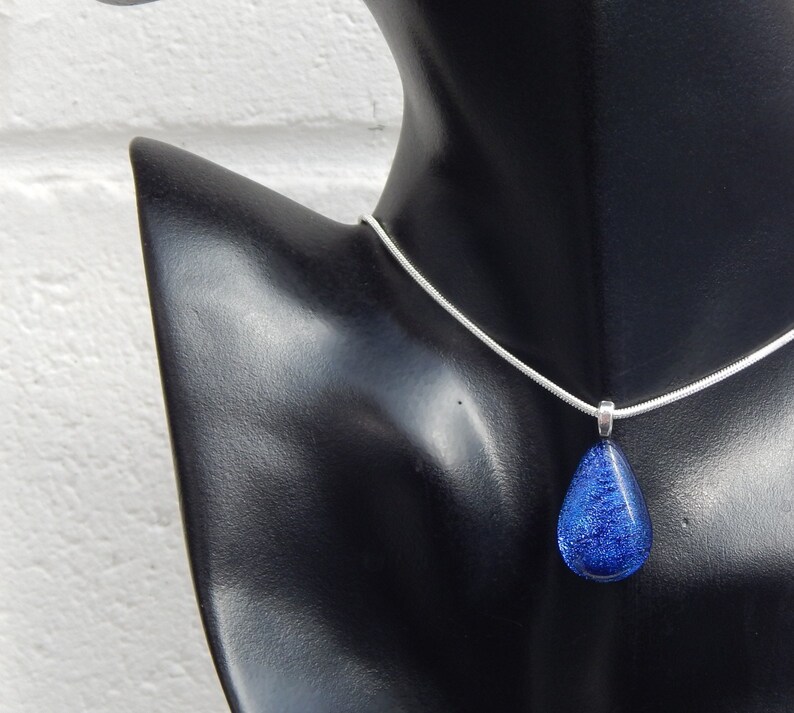 Puede incluir: Un collar de cadena de plata con un colgante en forma de l&aacute;grima de vidrio dicroico azul.