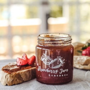 Könnte beinhalten: Ein Glas gefüllt mit selbstgemachter Erdbeermarmelade. Das Glas hat ein weißes Etikett mit der Aufschrift "Strawberry Jam homemade".