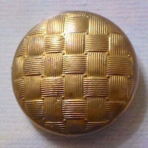 Könnte beinhalten: Ein goldfarbener Knopf mit einem gewebten Muster. Der Knopf ist rund und hat einen leicht erhöhten Rand.