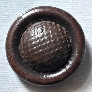 Könnte beinhalten: Ein dunkelbrauner Holz Knopf mit einer erhabenen, strukturierten, runden Mitte.