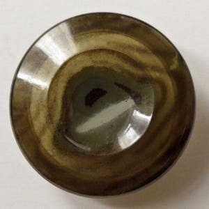 Può includere: Un bottone marrone e beige con un motivo a spirale. Il bottone ha una finitura liscia e lucida.
