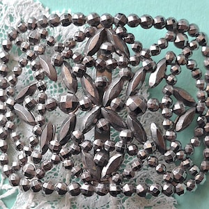 May include: A silver metal buckle with a decorative design of small, round beads and leaf shapes.