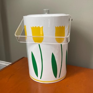 May include: White ice bucket with a clear plastic handle and lid. The bucket is decorated with yellow tulip flowers and green leaves on a white background. A yellow stripe accents the base.