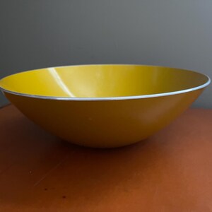 May include: A yellow bowl with a white rim. The bowl has a smooth, glossy finish and a rounded shape. The interior of the bowl is a bright yellow, and the exterior is a darker shade of yellow.