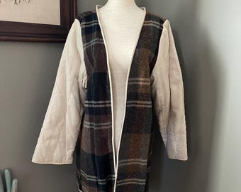 May include: A long-sleeved open-front jacket featuring a central panel of dark brown, black, and green plaid fabric. The sleeves and back are made of solid cream-colored quilted fabric. The entire garment is finished with a thin cream-colored trim.