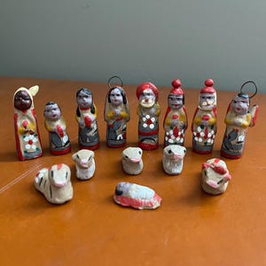 May include: A collection of small, hand-painted figurines, likely for a nativity scene. The figures include people and animals, with a variety of colors and designs. The figurines are arranged on a brown surface.