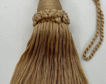 May include: A gold tassel with a long cord. The tassel is made of a soft, silky material and has a delicate, fringed design.