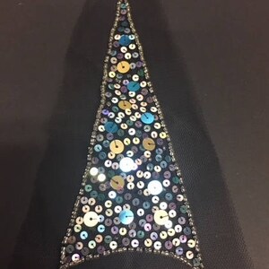 May include: A triangular-shaped fabric applique with a black background and a design of iridescent sequins in various shades of blue, green, and gold.