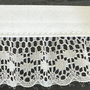 May include: White lace trim with a scalloped edge and a plain white fabric backing. The lace has a delicate floral pattern.