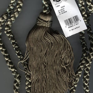 May include: A gray tassel with a braided cord. The tassel is made of a soft, woven fabric. The cord is made of a thick, braided material. The tassel is attached to the cord with a knot. The cord is about 1.5 meters long. The tassel is about 10 centimeters long. The tassel is about 5 centimeters wide. The tassel is made of 60% cotton and 40% polyester. The tassel is assembled in India. The label reads "Conso D97637 LBO 118844"
