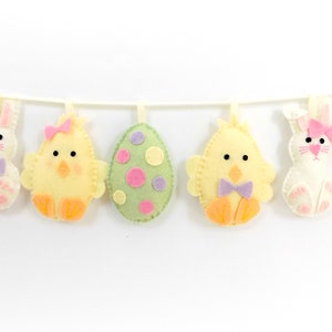 May include: A felt Easter garland with pink, yellow, green, and purple eggs and bunnies. The garland is strung on a white string.