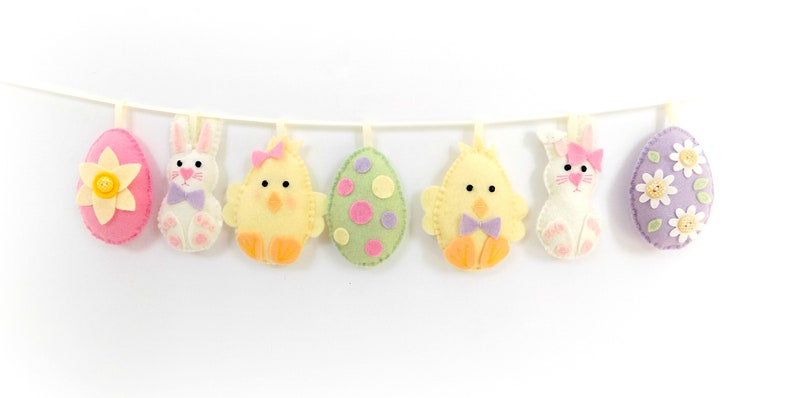 May include: A felt Easter garland with pink, yellow, green, and purple eggs and bunnies. The garland is strung on a white string.