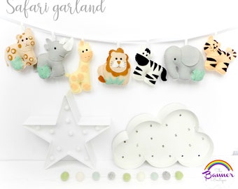 May include: A felt safari garland with a lion, zebra, elephant, giraffe, rhino, and tiger. The garland is hanging on a white wall with a white star and cloud light behind it.