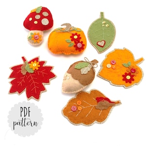 Puede incluir: Un conjunto de adornos de fieltro con temática otoñal, que incluye una calabaza, una bellota, un hongo y hojas. Los adornos están decorados con purpurina, botones y bordados. El texto "PDF pattern" es visible en la imagen.