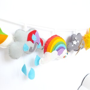 K&ouml;nnte beinhalten: Eine Filz-Girlande mit einem Regenbogen, Wolken, einer Sonne, einem Drachen und einer Gewitterwolke mit Blitz. Die Girlande ist an einer wei&szlig;en Schnur befestigt und eignet sich perfekt f&uuml;r ein Kinderzimmer oder ein Babyzimmer.