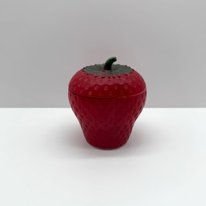 Peut inclure: Un pot en céramique rouge en forme de fraise, avec une tige et des feuilles vertes. Le pot a une surface texturée qui ressemble aux graines d'une fraise.