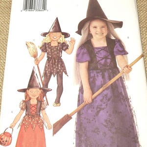 May include: Butterick sewing pattern 3242 for children's witch costumes. The envelope displays three variations of a dress with a pointed hat, featuring purple and orange fabrics with star and moon patterns, along with illustrations of broomsticks.