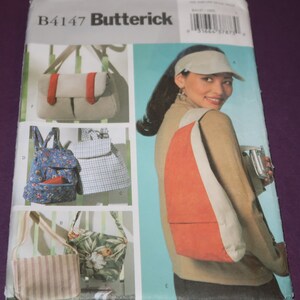 May include: A sewing pattern envelope featuring various bag designs. The bags include a beige messenger bag with a red strap, a floral backpack, a striped tote, and a tropical print handbag. The envelope also shows a woman wearing a red and white sling bag.