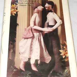 May include: A vintage pattern cover featuring two fabric dolls, a woman in a pink dress and a man in a white shirt and striped pants. The text reads "elinor peace bailey" and "Old Lady Original's Shady Lady and Dapper Dan."
