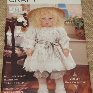 May include: A vintage Vogue Craft doll pattern for a girl doll wearing a white dress with lace trim, a straw hat, and white socks. The pattern is for one size and includes a full color iron-on transfer for the face.