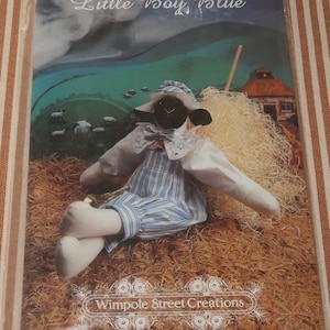 May include: A black and white sheep doll wearing blue and white striped overalls and a white hat. The doll is sitting on a bed of straw with a wooden stick and a small building in the background. The text "Little Boy Blue" is at the top of the image and "Wimpole Street Creations" is at the bottom.