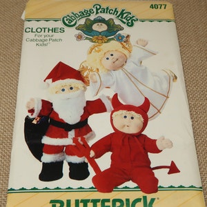 May include: A vintage Butterick pattern for Cabbage Patch Kids clothes. The pattern features illustrations of dolls dressed as Santa Claus, an angel, and a devil. The pattern's packaging is cream-colored with green and yellow accents.