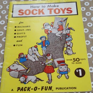 May include: A yellow instructional booklet titled How to Make SOCK TOYS, featuring a large brown sock illustration surrounded by various cartoon characters. The cover text includes BAZAARS, SHUT-INS, GIFTS, PROFIT, and FUN, with a $1 price tag.