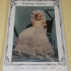May include: A sewing pattern for a doll dress for a 21-22 inch doll. The pattern is called "Yesterday's Children" and is for a white dress with lace trim. The pattern is from BS-164.