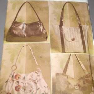 May include: Vogue Accessories pattern V8506 featuring four different handbag designs. The bags include a metallic bronze shoulder bag, a quilted tote with brown trim, a floral print shoulder bag, and a floral tote bag.