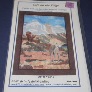 May include: A packaged craft pattern titled "Life on the Edge" featuring a mountain landscape with two animals. The pattern is 28" wide and 38" long. The pattern uses fusible web and raw edge appliqué techniques.