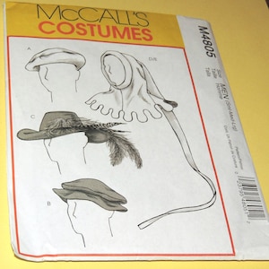 May include: A McCall's Costumes sewing pattern envelope M4805 featuring line drawings of various headwear styles including a flat cap, a wide-brimmed hat with feathers, and a hooded cowl with a long tail, labeled with sizes Sml-Med-Lrg.