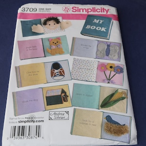 May include: Simplicity pattern 3709 for a fabric activity book. The cover features a colorful, open book with various interactive pages, including a shoe, a dog house, and a butterfly. The text "MY BOOK" is visible on the cover.