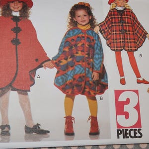 May include: A sewing pattern for three children's capes. The capes are in red, blue, and plaid patterns. The pattern includes instructions for making the capes.