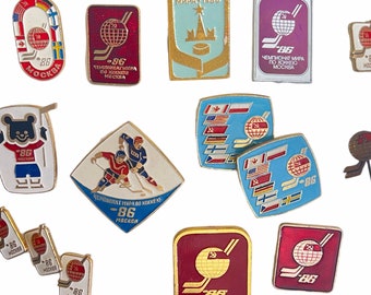 Puede incluir: Una colección de 13 pines de esmalte vintage que conmemoran el Campeonato Mundial de Hockey sobre Hielo de 1986 en Moscú. Los pines presentan una variedad de diseños, incluido el logotipo del campeonato, la mascota y las banderas de los países participantes.
