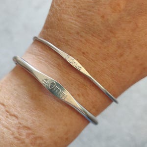 May include: Two silver crochet hooks, one marked "2.0mm" and the other "4.0mm". The hooks are thin and curved, designed for crafting. The image shows the hooks resting on a wrist.