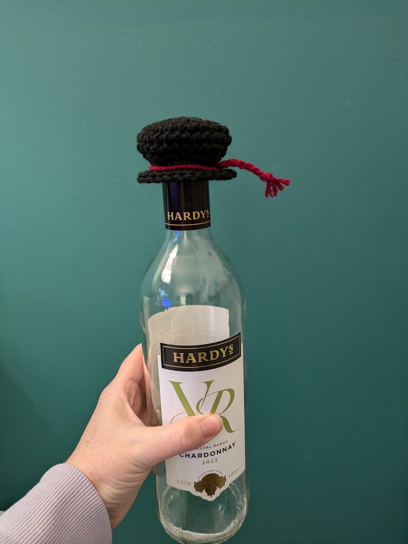 K&ouml;nnte beinhalten: Eine klare Glasflasche Hardy's VR Chardonnay Wein mit einem schwarzen geh&auml;kelten Flaschenverschluss mit einem roten Band.