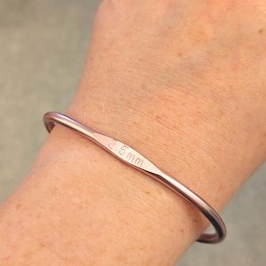 May include: A rose gold metal bangle bracelet with the inscription "3.5 mm" on the front.