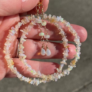 May include: A pair of gold hoop earrings with a double row of iridescent white opal chips. The earrings have a dangling drop of opal at the bottom.