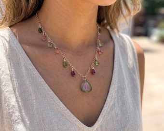 Könnte beinhalten: Eine goldfarbene Halskette mit einem Wassermelonen-Turmalin-Anhänger und kleinen, farbigen Edelstein-Akzenten. Die Halskette hat eine zarte Kette und wird um den Hals getragen. Die Edelsteine sind in verschiedenen Rosa-, Grün- und Lilatönen gehalten.