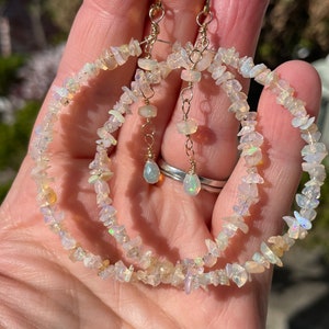 May include: A pair of gold hoop earrings with a dangling opal gemstone. The hoops are made of small, white opal chips.