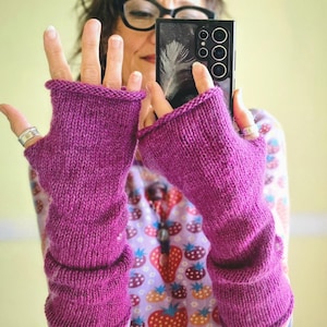 May include: A pair of vibrant magenta fingerless gloves crafted from a knitted yarn material. These long, arm-covering accessories feature a simple stockinette stitch pattern with rolled edges at the top and bottom openings.