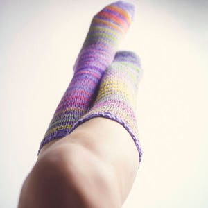 May include: A pair of colorful striped socks in shades of purple, pink, yellow, and green. The socks are knitted and have a soft, fuzzy texture.