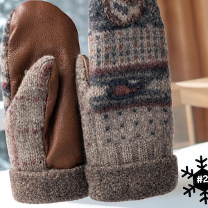 May include: A pair of winter mittens. The palms are brown leather, and the backs are knitted wool with a pattern of blue, red, and brown geometric shapes. The cuffs are a solid brown colour.
