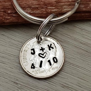 May include: A personalized keychain featuring a silver dime with the initials "J + K", a heart symbol, and the date "4/10" stamped on it. The dime is attached to a silver keyring.